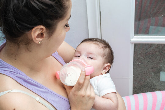 Beautiful Latina Woman Looking At Her Two Month Old Baby As She Feeds Her And She Starts To Fall Asleep In Her Arms. Tender Baby With Her Eyes Half Closed About To Fall Asleep. Concept Of Motherhood.