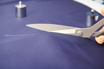 Tailor cutting blue fabric with scissors on the table. Clothes sewing. Tailoring. Close up view