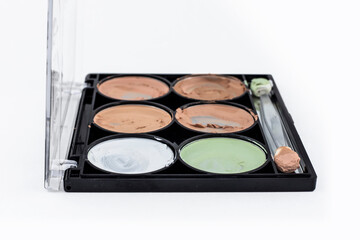 A palette of concealers to hide minor flaws in makeup. Six colors of body correctors, green and white. Careless use of the palette. White background.