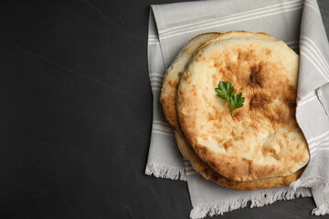 Delicious fresh pita bread with napkin on black table, top view. Space for text