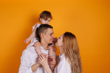 Cute family of father, mother and daughter smiling, playing and joking together. Woman and man kisses and embraces. Happy family with a baby girl on hands kissing daughter