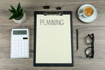 Flat lay composition of clipboard with word Planning, calculator, eyeglasses, coffee, pen and houseplant on wooden table