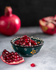 pomegranate seeds in a dark bowl on light grey background