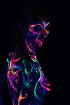 Naked woman on her back in a pitch-black room with her skin painted with fluorescent paint. 