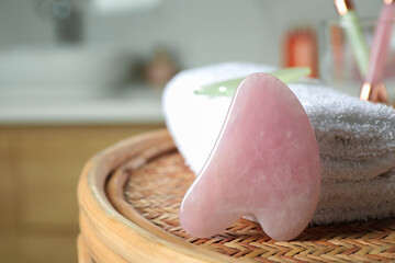 Rose quartz gua sha tool and soft towel on wicker table indoors, closeup. Space for text