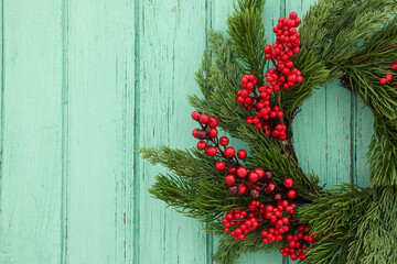Fototapeta na wymiar Beautiful Christmas wreath with red berries hanging on turquoise wooden wall, closeup. Space for text