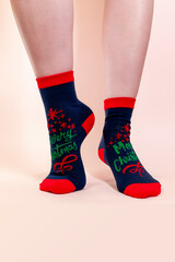 A woman in Christmas socks stands on her toes on a pink background. Blue socks with the inscription merry Christmas