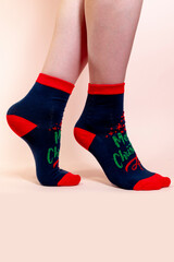 A woman in Christmas socks stands on her toes on a pink background. Blue socks with the inscription merry Christmas