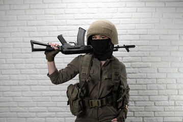 A Ukrainian girl soldier in a helmet and military ammunition with a Kalashnikov assault rifle on the background of a brick wall