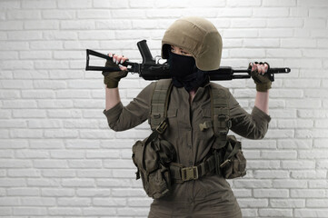 A Ukrainian girl soldier in a helmet and military ammunition with a Kalashnikov assault rifle on the background of a brick wall