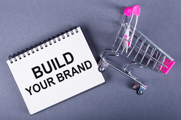 Text BUILD YOUR BRAND printed on a notepad lying next to a shopping trolley. Business concept