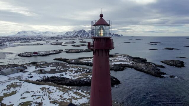 Beautiful aerial pedestal shot of the Andenes Lighthouse in Norway with the snow speckled rocky shore and mountains in the background