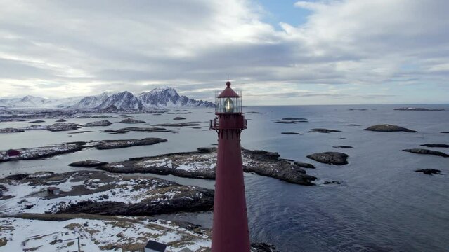 Ariel horizontal orbit of the Andenes lighthouse  with stunning views of the rocky coast and snow covered mountains, with the light flashing