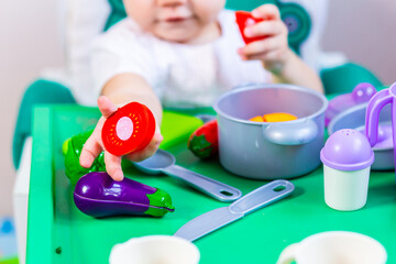 Blurred little child holding a toy vegetable in his hands on the background of dishes