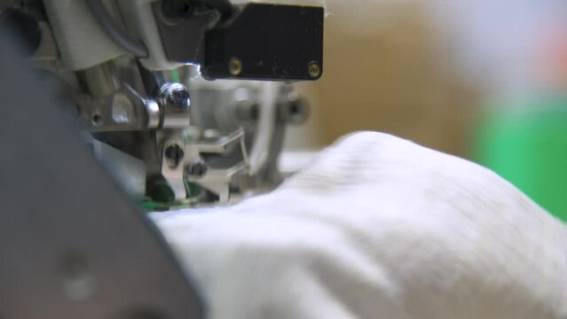 Close-up of overlock foot and cutter overlocking cuff in glove manufacturing. . The overlock machine trims the edges of the fabric. garment factory