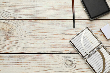 Cigarettes, holder, cases and matchbox on white wooden table, flat lay. Space for text