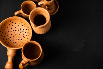 Clay pots for cooking. Light clay clay pots. Baking tins on a dark background. Earthenware: colander, plate, grocery, candlestick. Vintage kitchen utensils for cooking.