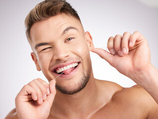 Flossing keeps you fresh. Studio shot of a young man flossing his teeth against a grey background.