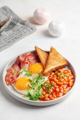 Continental breakfast - eggs, toast, bacon and beans in tomato sauce on a plate on the table.