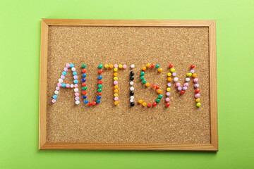 Corkboard with word Autism made of colorful pins on light green background, top view