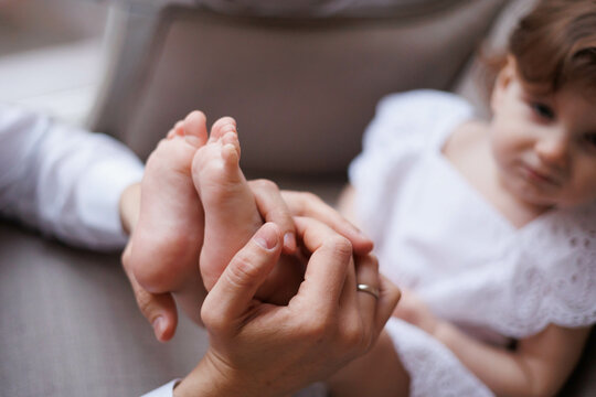 Closeup of little baby girl's feet in hands of her father. Fingers of man playing with girl's feet. Hands holding small daughter's legs, tenderly and accurately
