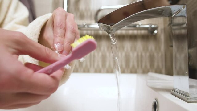 Close-up of unrecognizable caucasian young woman toothbrushing her kappa aligner under running water in bathroom sink. Care of dental accessories