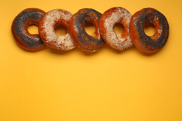 Many delicious fresh bagels on orange background, flat lay. Space for text