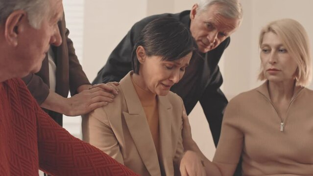 Medium slowmo of despaired mature woman crying during support group meeting, seeking for emotional help and support from other group members comforting her