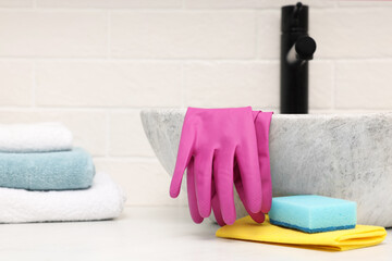 Sponge, rag and rubber gloves near sink in bathroom. Space for text
