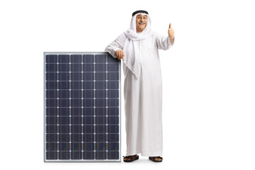 Full length portrait of an arab man in ethnic clothes leaning on a solar panel and showing thumbs up