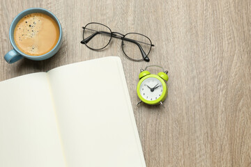 Open notebook, glasses, alarm clock and cup of coffee on wooden table, flat lay. Space for text