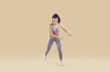 Fototapeta na wymiar Beautiful fit woman in activewear having a cardio gym workout. Athletic fitness trainer in modern sportswear doing jumping exercises. Full length studio shot, isolated on a beige colour background