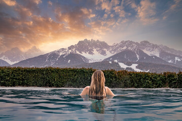 Woman relaxing in swimming pool against snowcapped mountains during sunset
