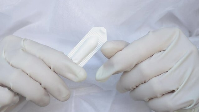 Suppositories in woman hands, white gloves. nurse or doctor, medical assistant, in white disposable robe holds a suppository in plastic pack. Suppository for anal or vaginal use. temperature, fever