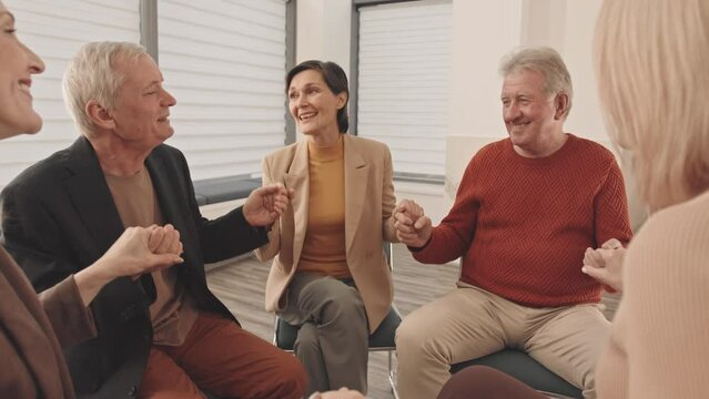 Medium slowmo of group of inspired cheerful adults and therapist saying affirmations all together and holding hands during support group meeting