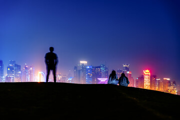 Blurred silhouette of a standing man and two young women against the backdrop of the night city of...