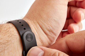 Fototapeta premium Man fastens a multifunctional fitness bracelet on his wrist on a white background. Smart technology helps people.