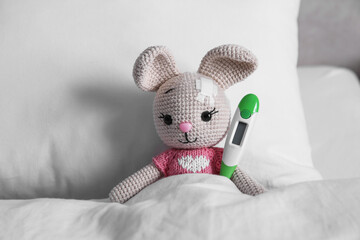 Cute toy bunny with sticking plaster and thermometer in bed. Children's hospital