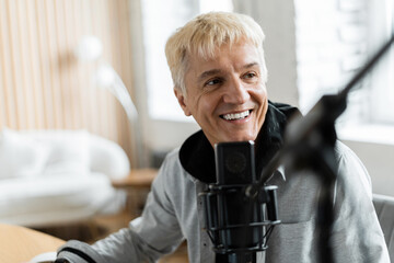 An adult male works as a presenter at a radio station , broadcasts using a microphone and a laptop
