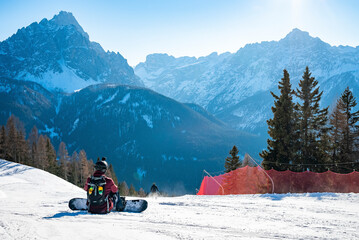 Rear view of tired snowboarder sitting on snowy landscape against mountains