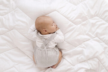 newborn baby in white bodysuit and gray romper sleep sweet on his tummy on white blanket, cute baby sleep top view