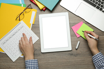 Woman writing note while using tablet for online studying at wooden table, top view. Distance learning