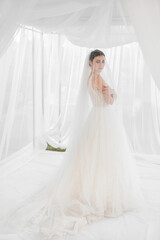Happy bride with a beautiful long veil and a wedding bouquet. White curtains