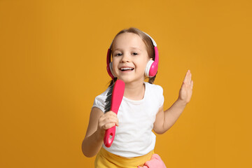 Cute little girl in headphones with brush singing on orange background