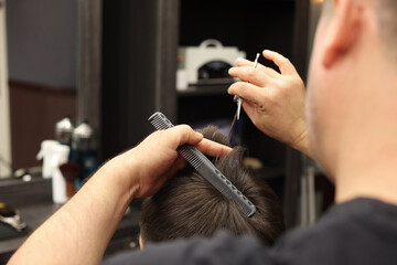 Professional hairdresser cutting man's hair in barbershop, closeup