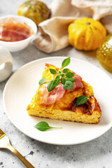 A piece of frittata with pumpkin, bacon and ricotta in a ceramic plate on a light culinary background. Traditional Italian delicious homemade egg dish on the kitchen table closeup	
