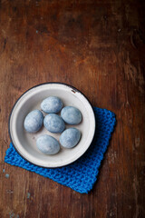 Easter eggs painted blue in white bowl on brown wooden background. Vertical shot, top view on countryside table.