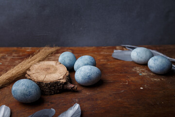 Blue painted easter eggs on brown wooden table with decorative silver feathers. Copy space
