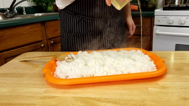 Home cooking - Pouring and spreading vinegar mix with sugar and salt ang kombu preparing rice for sushi.