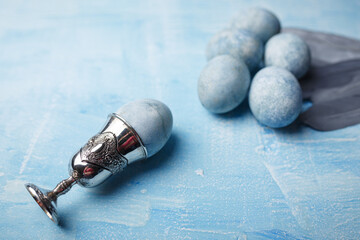 Beautiful painted easter eggs and silver feathers on blue background. One Easter egg in egg cup. Close up shot